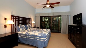 A bedroom with a bed, nightstands, a ceiling fan, a TV, and a sliding glass door to a balcony.