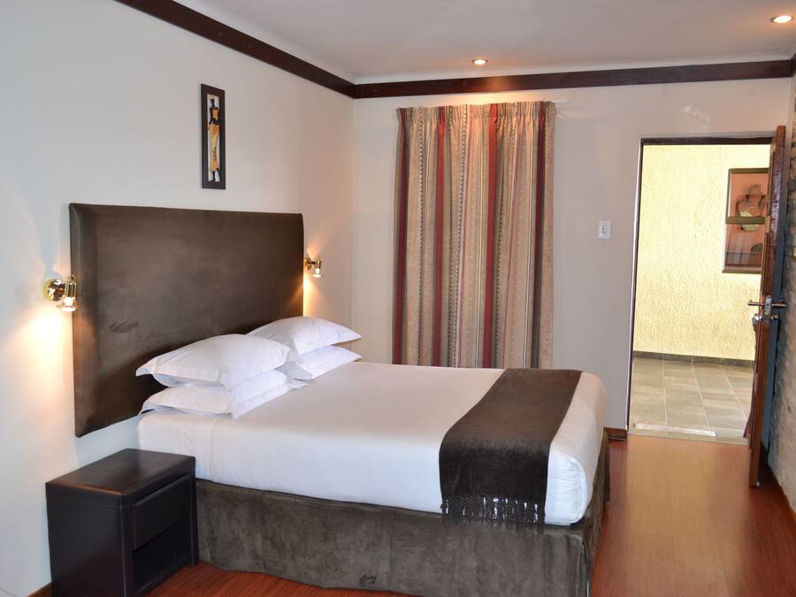 Habitación de hotel con una cama grande, una mesita de noche, cabecera, cortina y puerta que da a un baño.