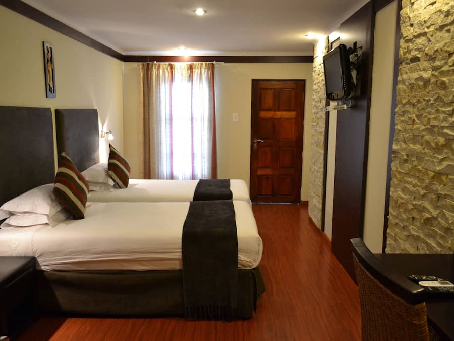 A hotel room with two beds, a television, a stone wall, and a wooden floor.