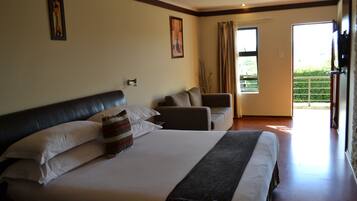 A hotel room with a large bed, a sofa, a window with curtains, and a door leading to a balcony.