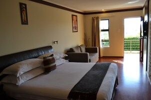 Habitación de hotel con una cama grande, un sofá, una ventana con cortinas y una puerta que da a un balcón.