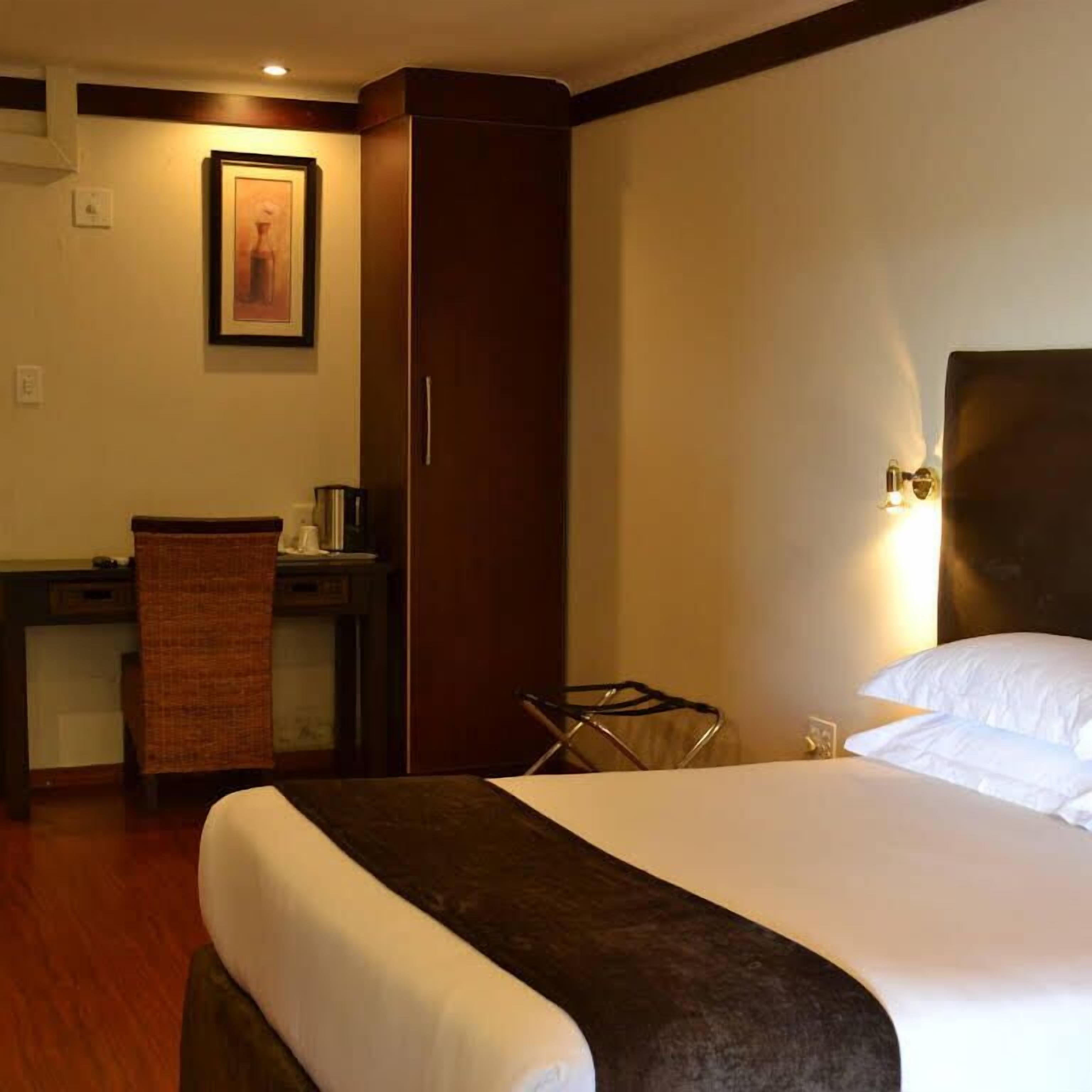A hotel room with a bed, a desk, a chair, a wardrobe, and a framed picture on the wall.