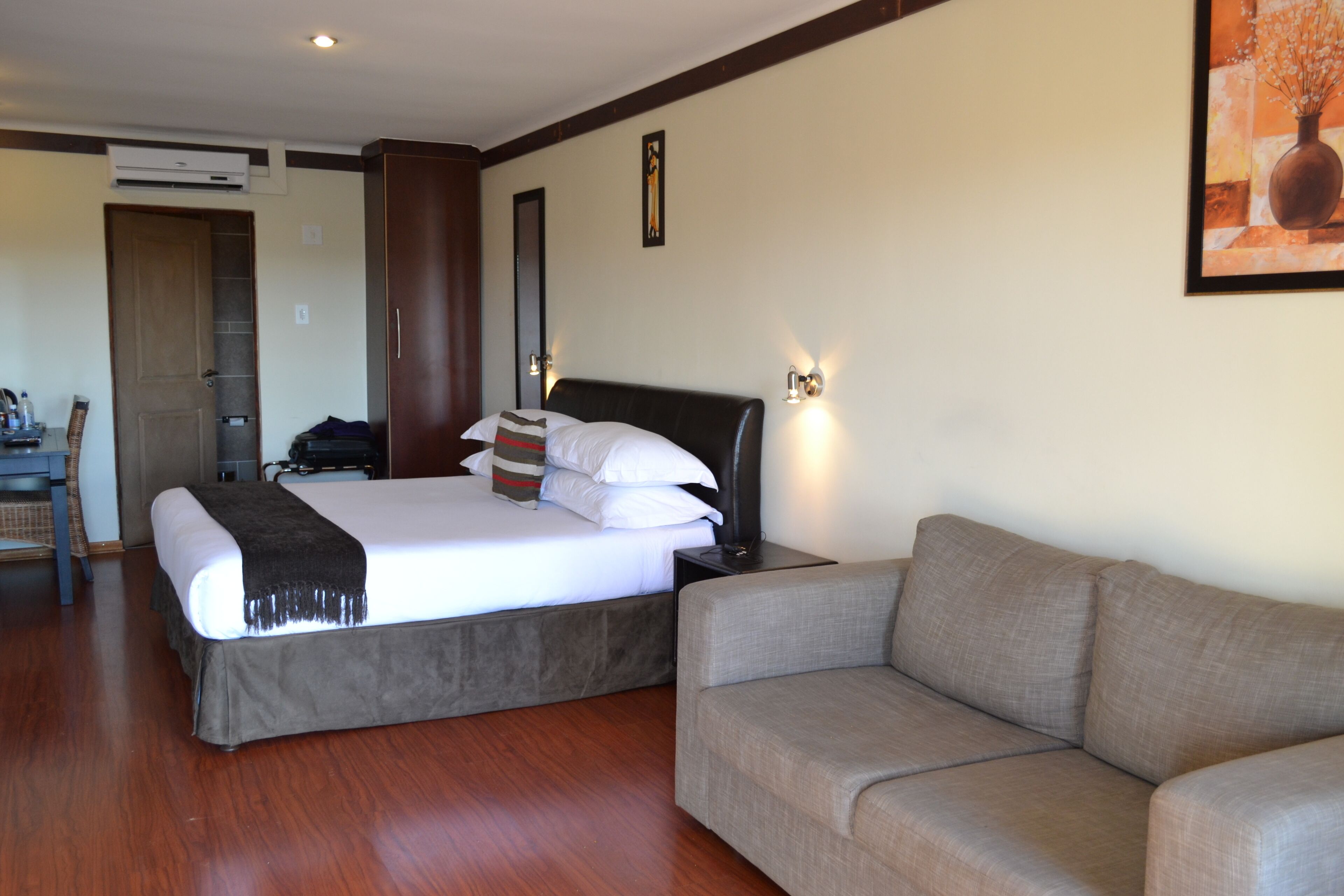 Een hotelkamer met een bed, een bank, een bureau en een airconditioning.