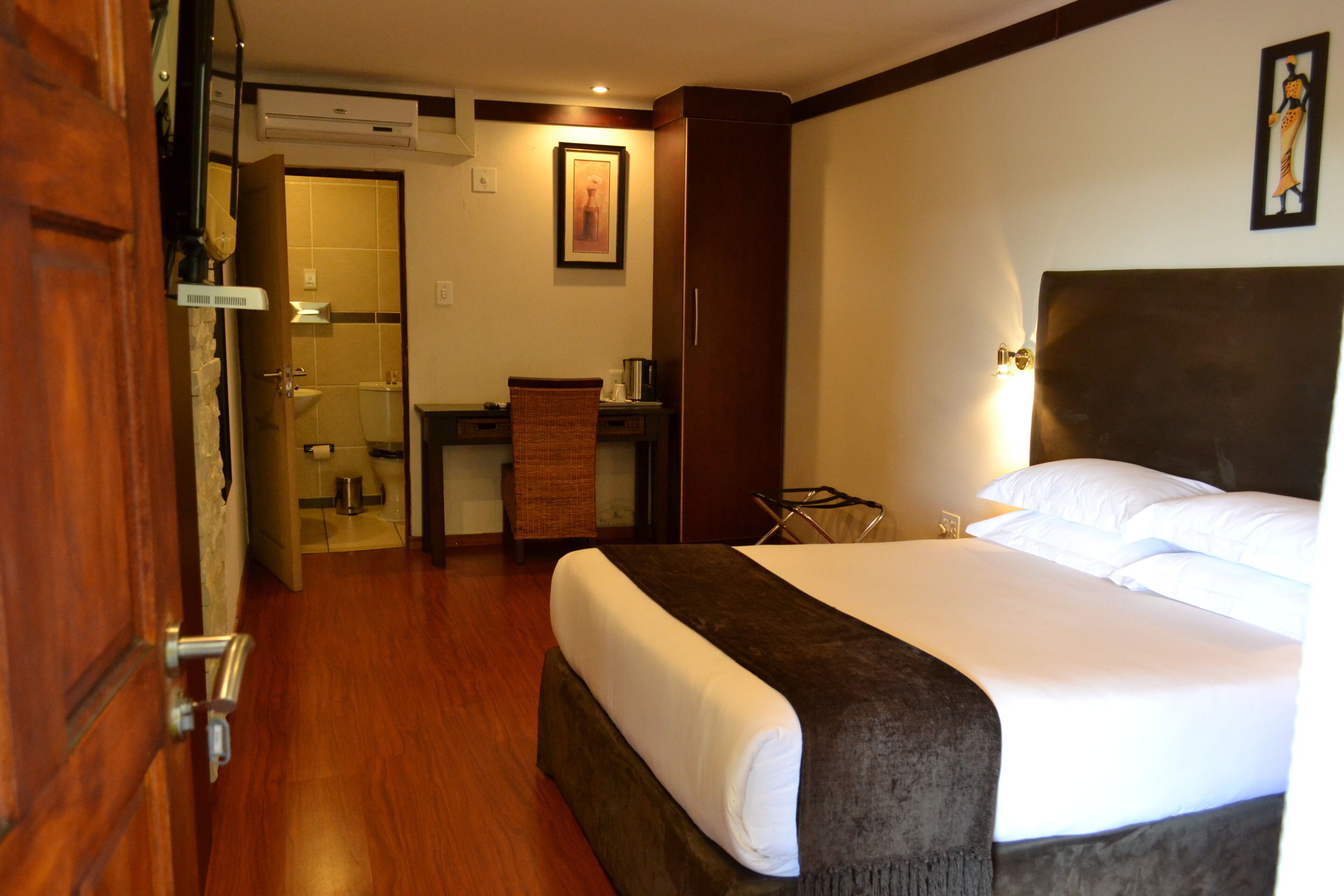 Habitación de hotel con cama, escritorio, silla, mesita y baño visible a través de una puerta abierta.