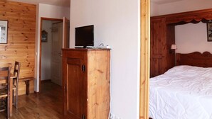Una habitación con paneles de madera, una cama, un televisor sobre un mueble de madera y una puerta que da a otra habitaci ón.