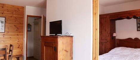 A wooden-paneled room with a bed, a television on a wooden cabinet, and a door leading to another room.