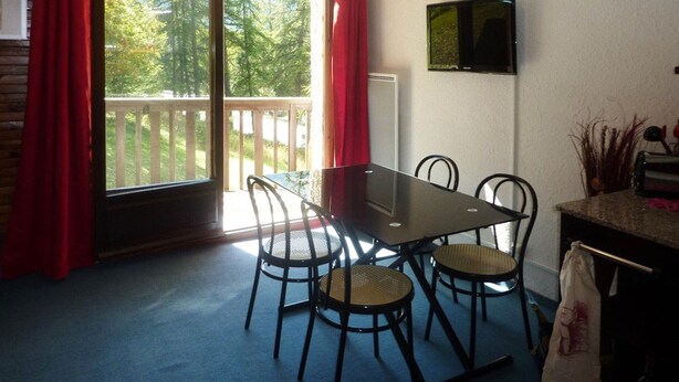 A dining area with a table and chairs, a television on the wall, and a view of the outdoors through a sliding door. - Comfortable Studio 4 Pers, Near Station and Chairlift, Les Orres (Les Orres)