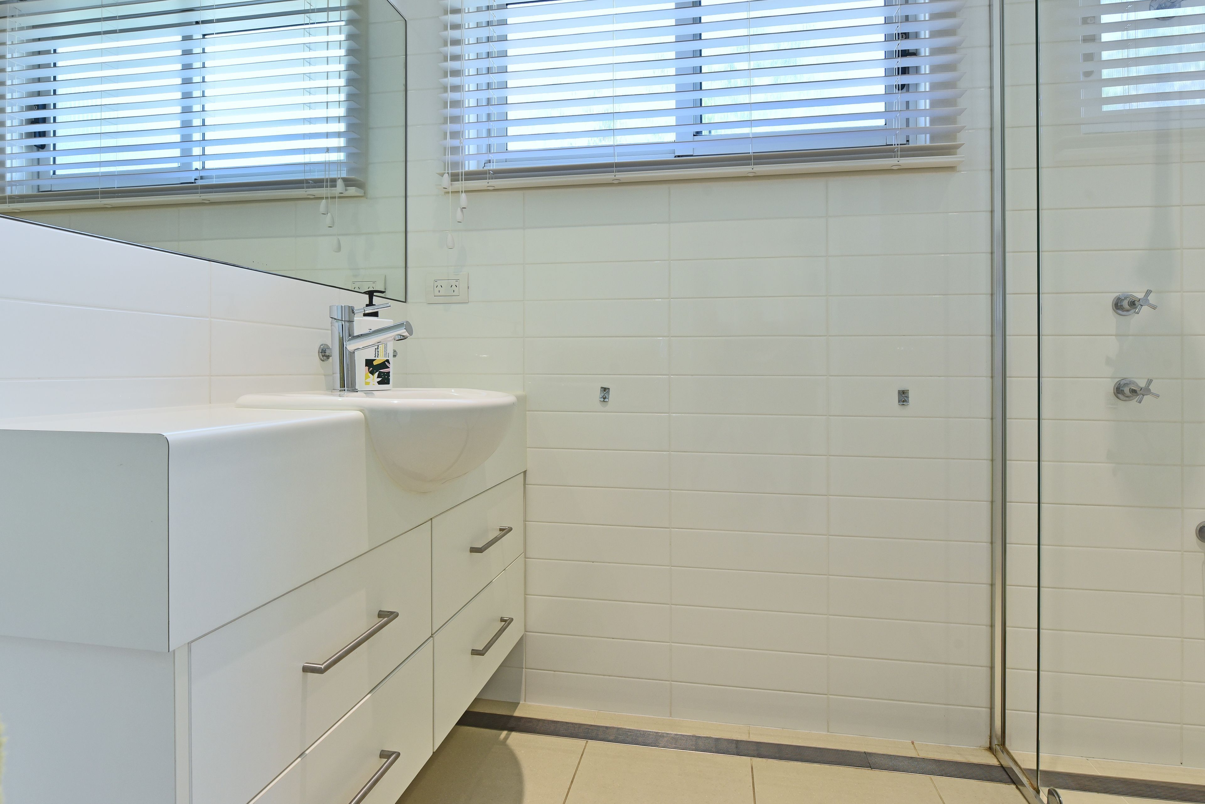 A modern bathroom with a white sink, mirror, and a glass shower enclosure.
