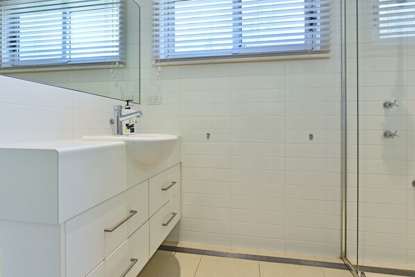 Une salle de bain moderne avec un lavabo blanc, un miroir et une douche en verre.