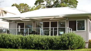 Ein Wohnhaus mit überdachter Veranda, großen Fenstern und einem gepflegten Rasen.