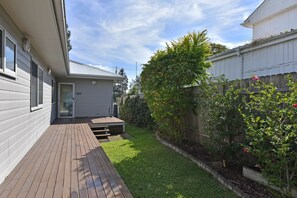 Ein Wohnhausgarten mit einer Holzterrasse, einem kleinen Garten und einem weißen Zaun.