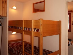 A bunk bed with striped bedding, a wooden headboard, and a mirror on the wall.
