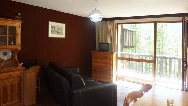 Un salon chaleureux avec un canapé, un meuble en bois, un téléviseur posé sur un meuble, et une table à manger avec des chaises.