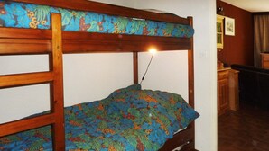 Un lit superposé avec une couvre-lit à motifs floraux, une tête de lit en bois et un bureau avec une chaise dans la pièce adjacente.