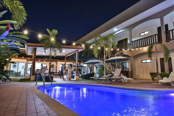 An outdoor swimming pool area with lounge chairs, umbrellas, and a covered seating area.