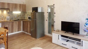A compact kitchen with a refrigerator, microwave, and coffee maker. There's a wooden dining table and a TV on a stand. - Cozy studio 5 pers, direct slope access, southwest balcony (Les Orres)