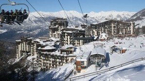 A ski resort with multiple buildings, including a large hotel with multiple floors and balconies, ski lifts, and a snowy landscape with mountains in the background. - Cozy studio 5 pers, direct slope access, southwest balcony (Les Orres)
