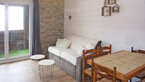 A cozy living room with a sofa, a dining table, and chairs. There is a large window with a view of a garden. - Cozy studio 5 pers, direct slope access, southwest balcony (Les Orres)