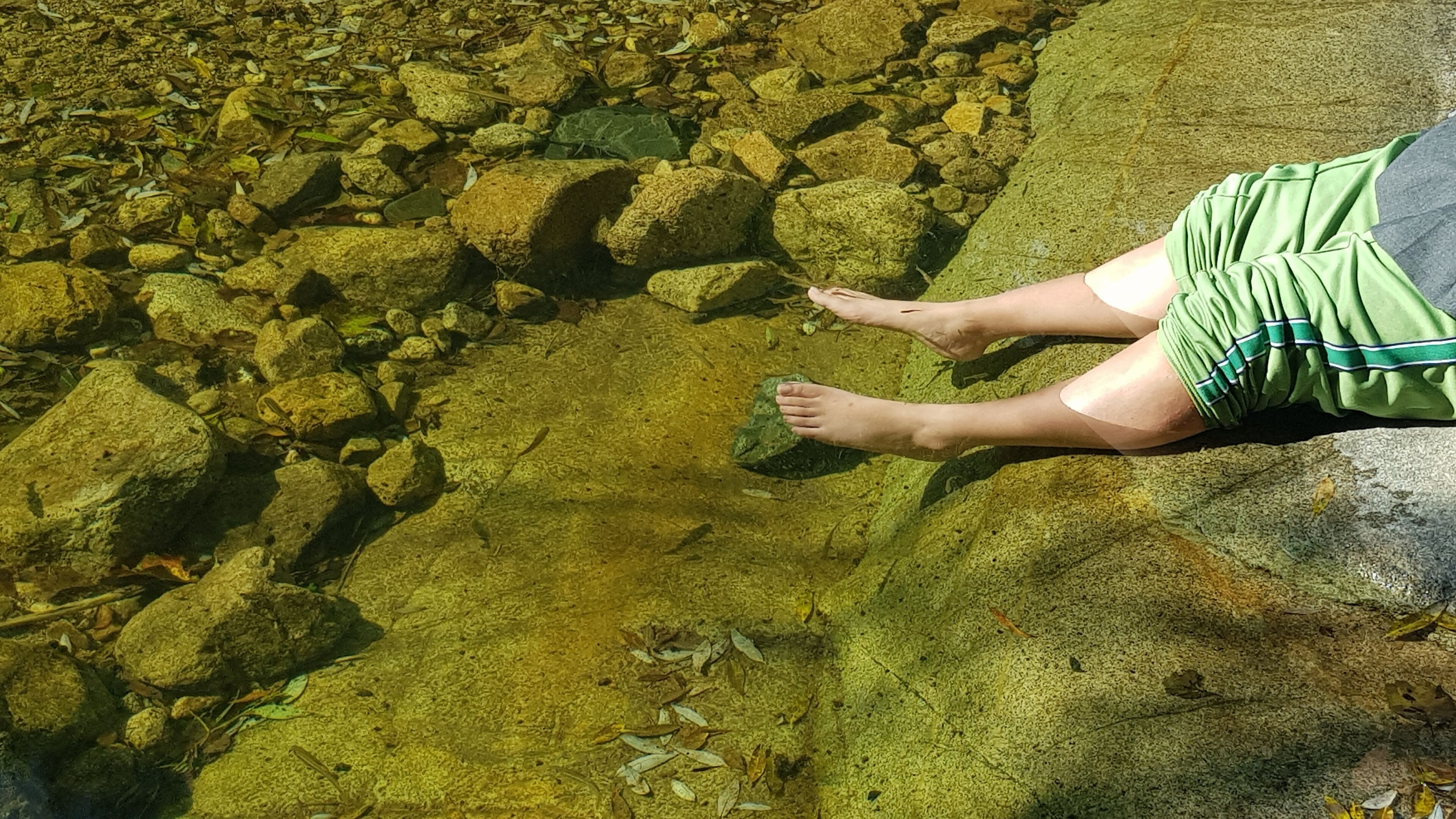 Une personne est assise sur un rocher, près d’une étendue d’eau claire où l’on peut voir des rochers et des feuilles.