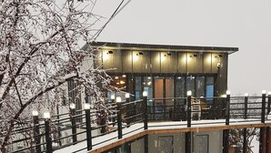Un edificio moderno con un espacio exterior cubierto, una terraza de madera y una barandilla de metal.