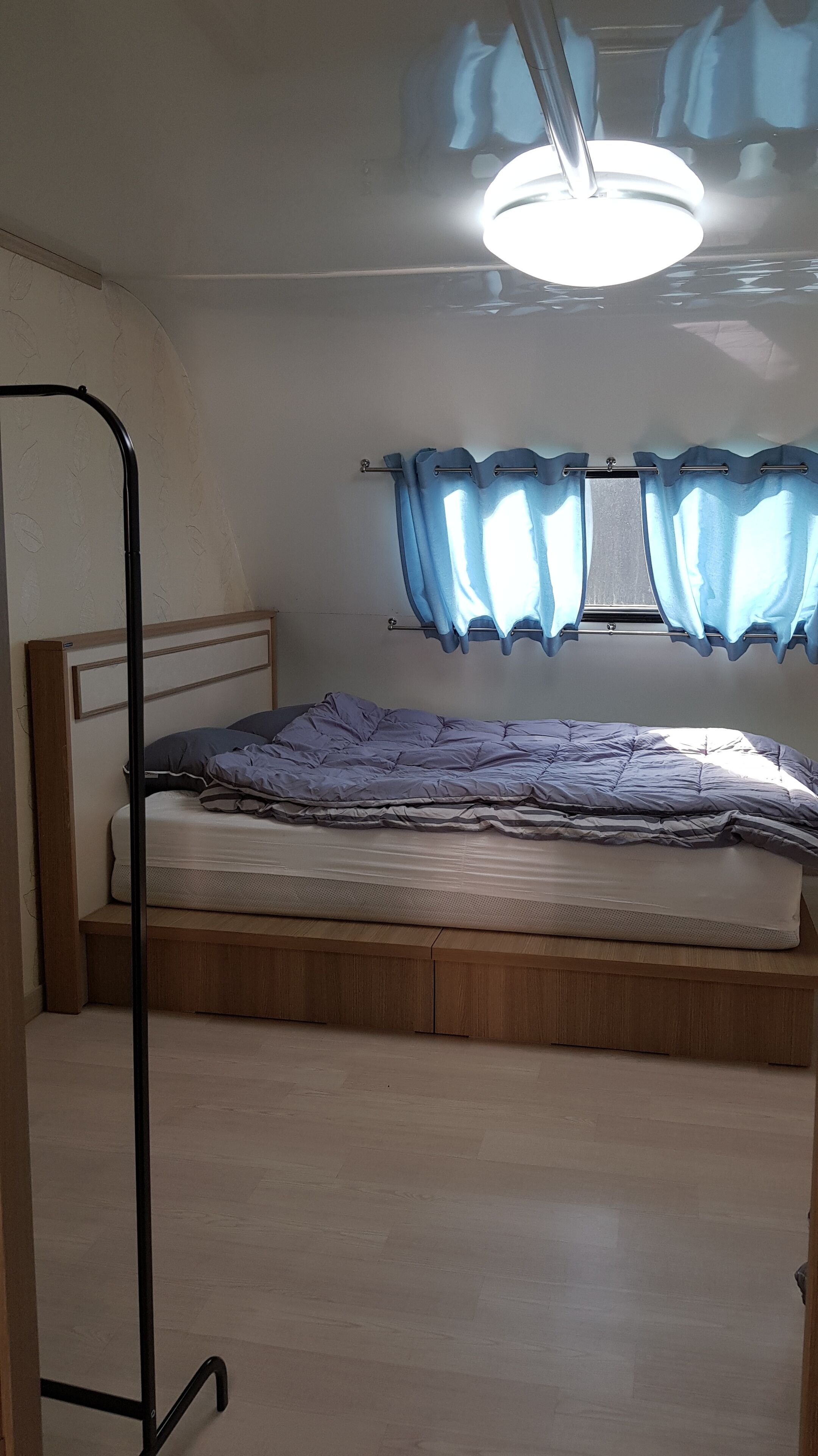 Uma cama de solteiro com cabeceira de madeira, mesa de cabeceira e janela com cortinas azuis.