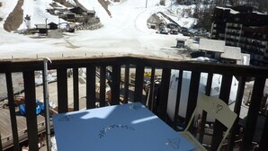 A snowy mountain view with a ski lift, buildings, and a wooden deck with a table and chairs. - Renovated studio, ski-in/ski-out, south-facing balcony (Les Orres)