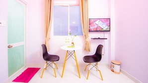 A small room with a window, two black chairs, a small table with a plant, a television on the wall, and a trash bin. - Saigon House 18Bis (Ho Chi Minh City)