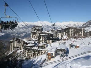 A ski resort with multiple buildings, including a large hotel with multiple floors and balconies, ski lifts, and a snowy landscape with mountains in the background. - Garden-Level Studio for 4 with Ski-In/Ski-Out Access and SW Terrace (Les Orres)