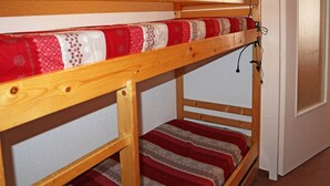 En køjeseng med træramme og sengelinned i rødt og hvidt.