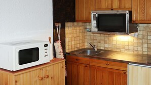 Et kompakt køkken med træskabe, en hvid mikrobølgeovn og en dobbeltvask.