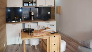 A compact kitchen with a microwave, coffee maker, and a small sink. There is a wooden table with a bottle, glasses, and a plate. The room has a wooden floor and a light-colored wall. - Newly Renovated Studio for 2 in Central Location with Direct Slope Access, Balcony & Stunning Views (Les Orres)