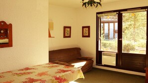 Ein Zimmer mit Bett, einer Bank, einem Sofa und einem Fenster mit Blick ins Grüne.