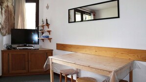 Una habitación con una mesa de madera, un televisor sobre un mueble de madera y un espejo en la pared.