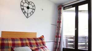 Una habitación con cama, un reloj con forma de corazón en la pared y vistas a través de un ventanal corredera.