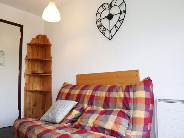 A room with a wooden bed, a heart-shaped wall clock, and a wooden shelf unit.