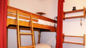 Habitación con literas, una escalera, un estante con un jarrón y una mesita.