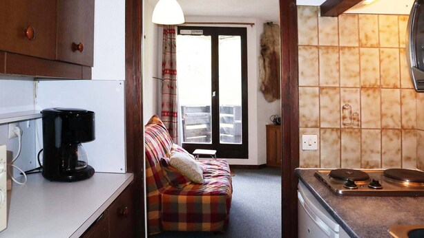 Una cocina compacta con cafetera, estufa y un comedor con sofá.