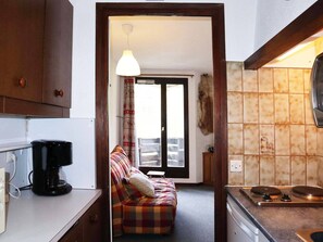 A compact kitchen with a coffee maker, a stove, and a dining area with a sofa.