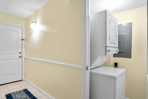 A room with a white door, beige walls, a white washing machine, and a small cabinet. - Oceanfront 2nd Floor. Outdoor Pool, Sundeck, Free Wifi | Crescent Sands CB - K2 (North Myrtle Beach)