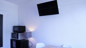 A small room with a TV mounted on the wall, a microwave on a shelf, a table, and two chairs. - Lovely studio for 4, ski-in/ski-out, wifi, pets allowed (Les Orres)