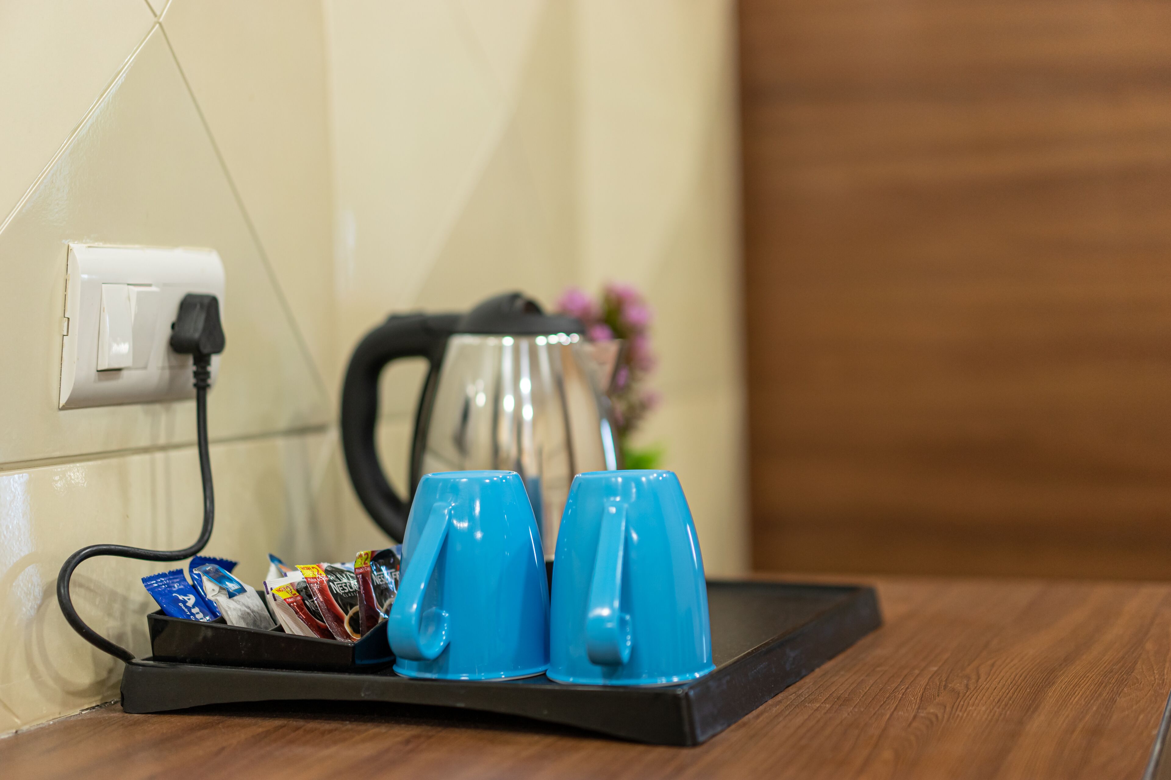 Una bandeja con dos tazas azules, una tetera y un enchufe sobre una mesa de madera.