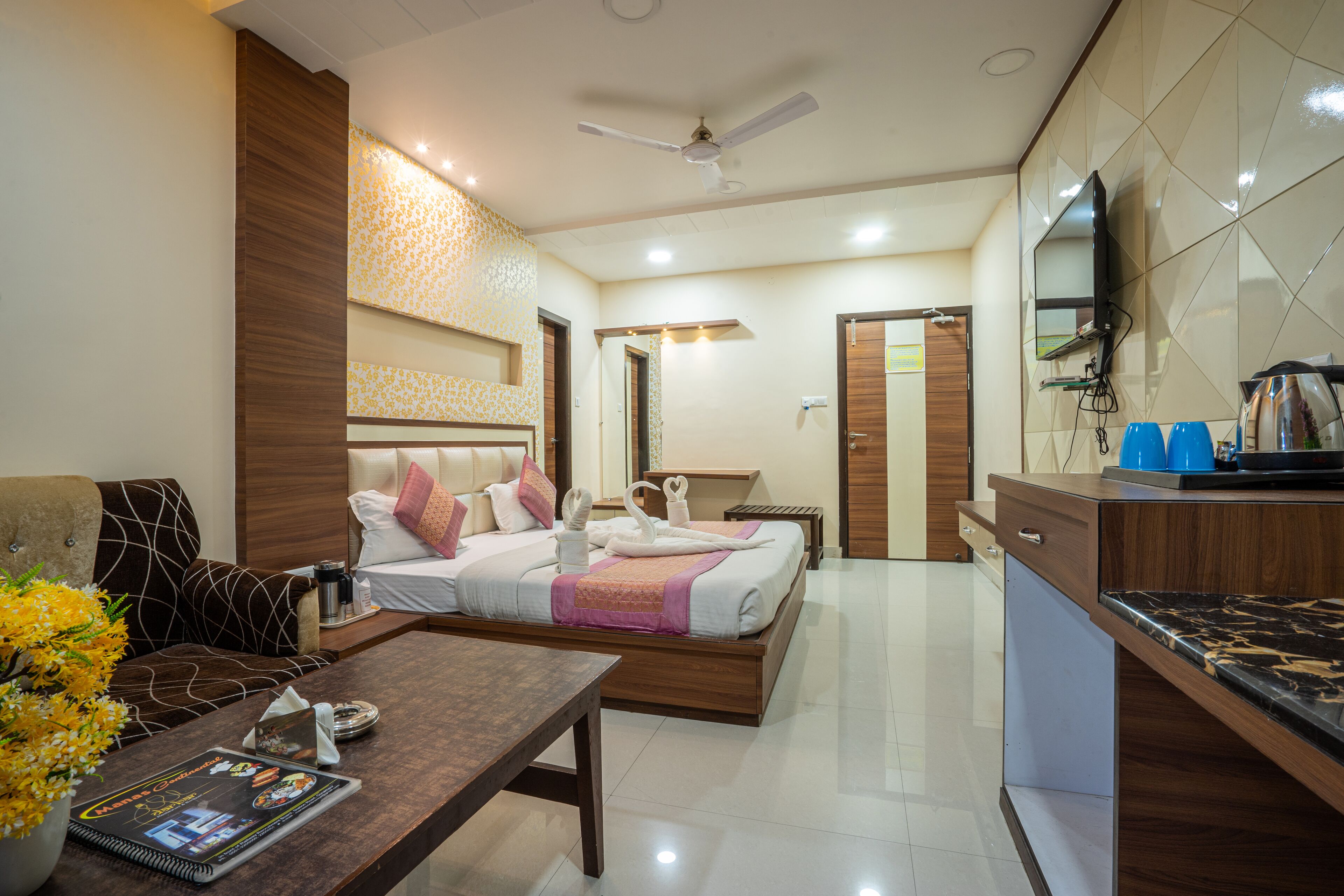 A modern hotel room with a bed, a sofa, a dining table, and a kitchen area.