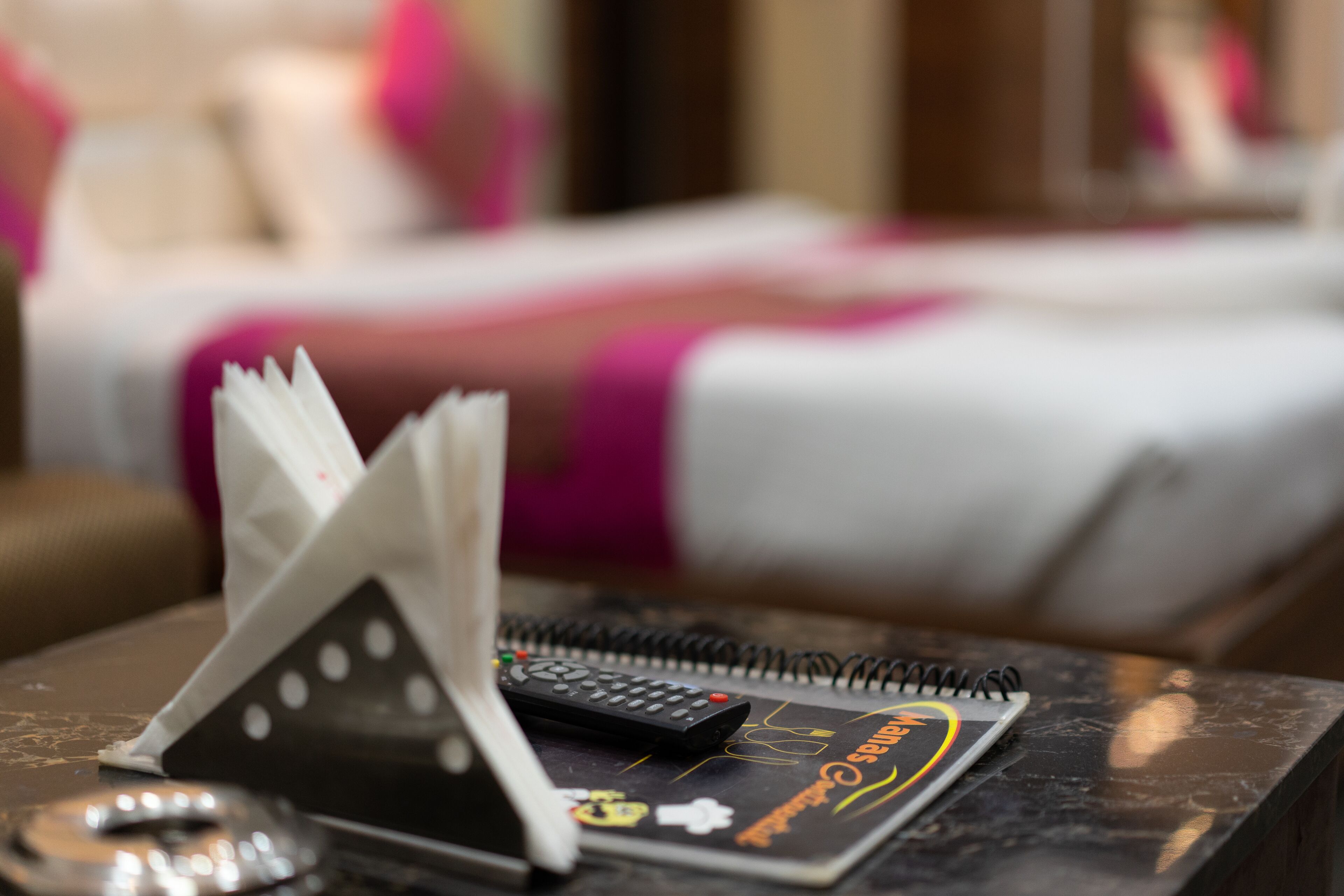 Une chambre d’hôtel avec un lit en arrière-plan, un carnet, une télécommande et une clé sur la table.