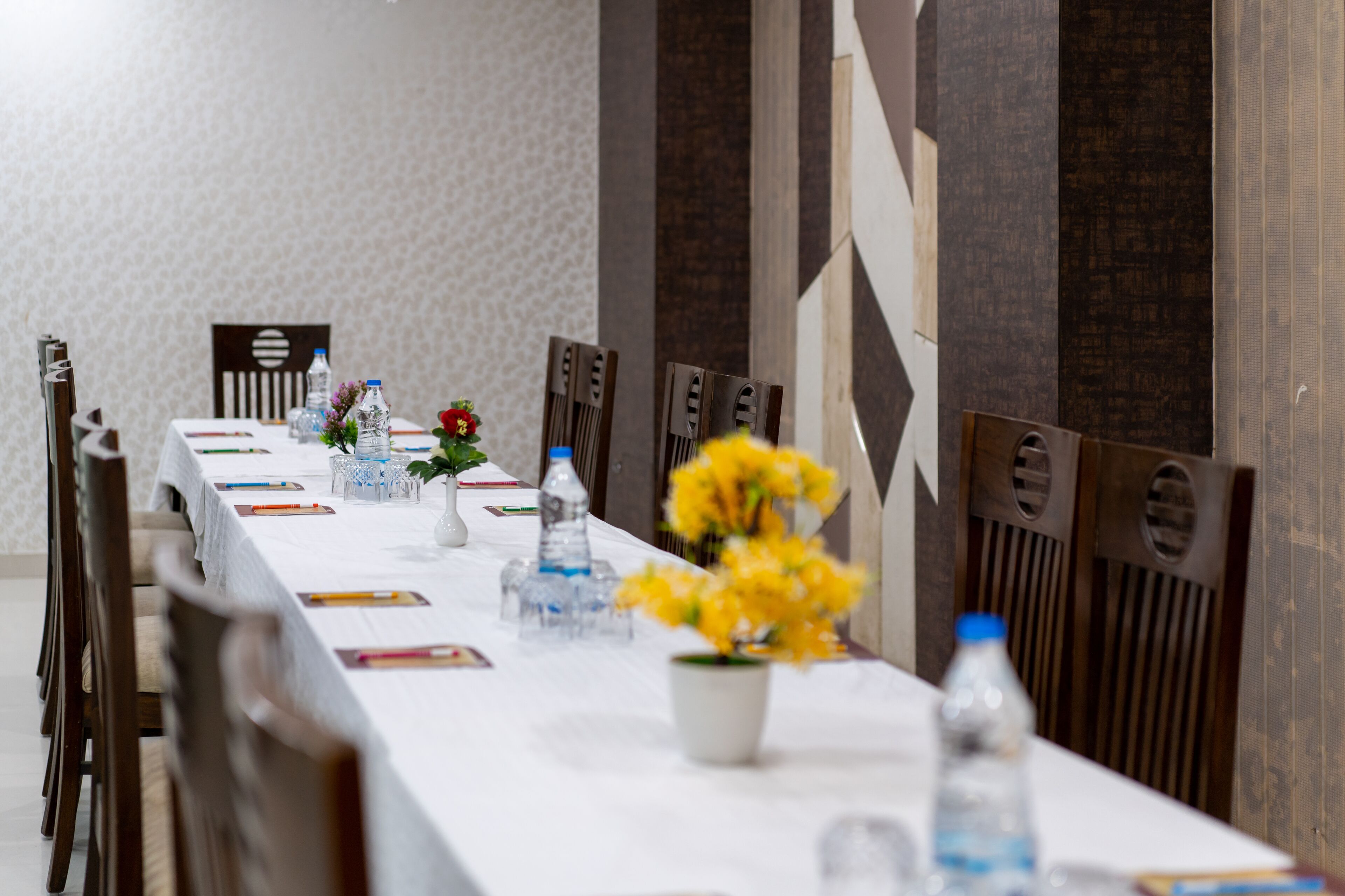 A conference room with a long table, chairs, water bottles, and a vase with yellow flowers.