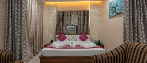 A hotel room with a bed, a ceiling fan, a wall-mounted air conditioner, and striped sofas.