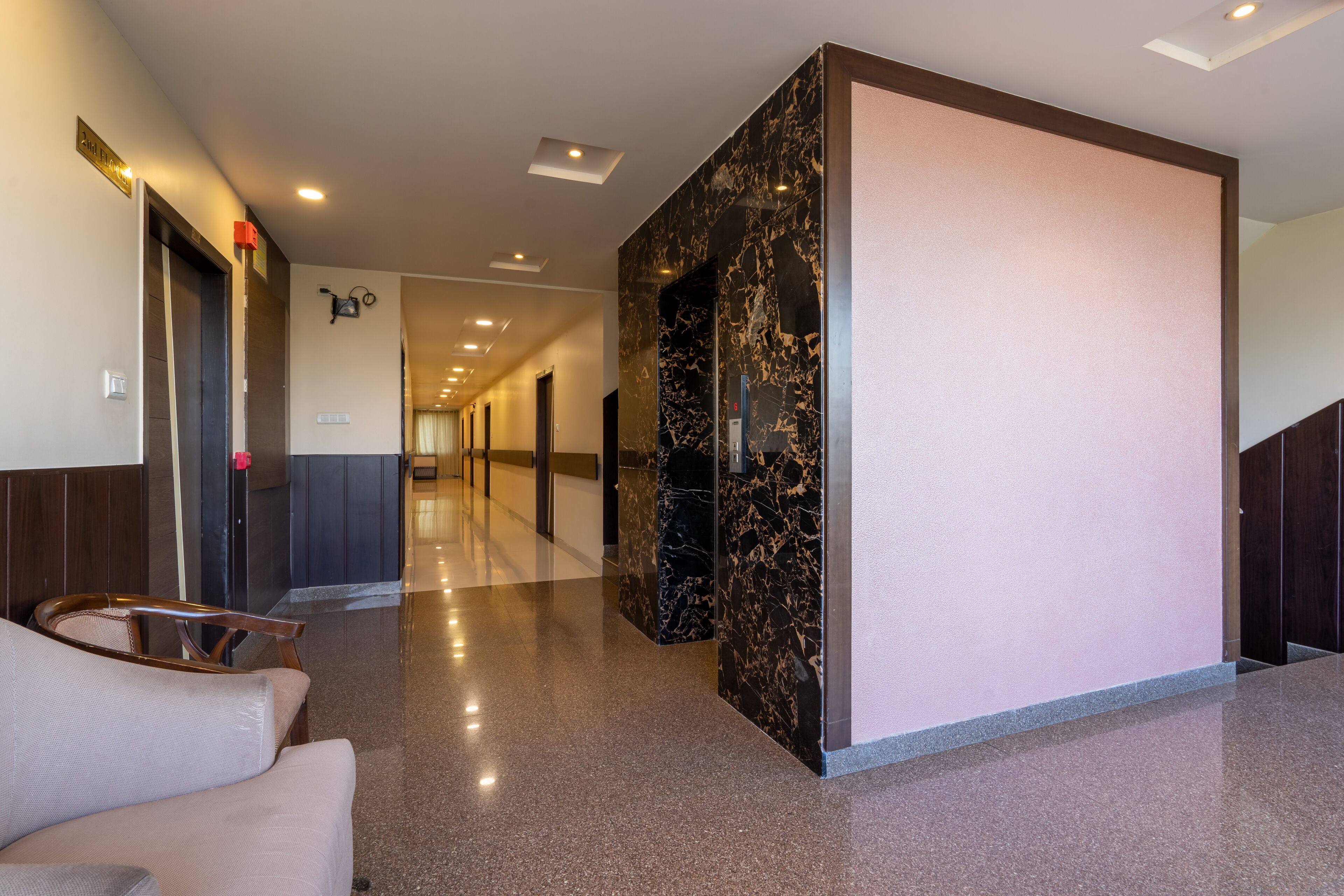 A hotel lobby with a marble reception desk, a seating area with a chair, and a staircase.