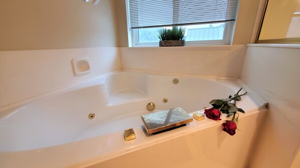 Una vasca da bagno con una finestra sopra, una piccola pianta e alcuni articoli da toilette sul lato.