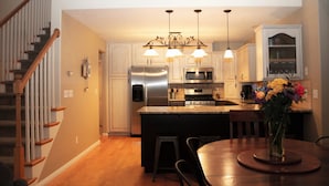 Una cocina moderna con una isla central, electrodomésticos de acero inoxidable, iluminación colgante y un comedor con una mesa redonda.