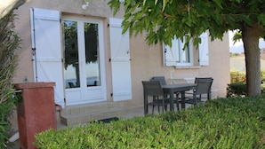 A building with a patio area featuring a table and chairs, a red planter, and a door with white shutters. - rental in the gulf of valinco in Propriano (Propriano)