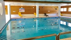 Una piscina interior con agua cristalina, rodeada de sillas de descanso blancas y amarillas, y paneles de madera.